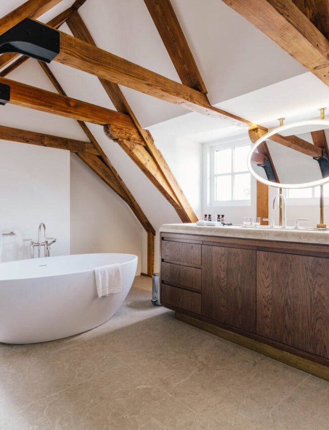 Bathroom in a Loft style suite at boutique hotel The Dylan Amsterdam, with a fee standing bath, exposed beams and a marble and wood console.