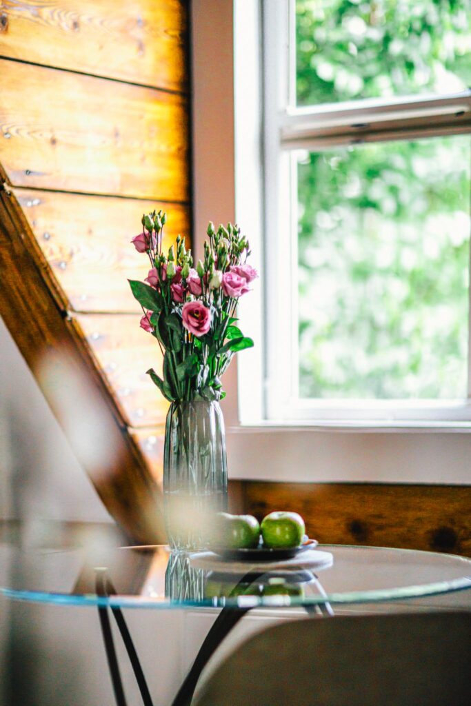 A table with a vase with pink rose flowers and three green apples on it, in a room at luxury boutique hotel The Dylan Amsterdam, member of The Leading Hotels of The World.